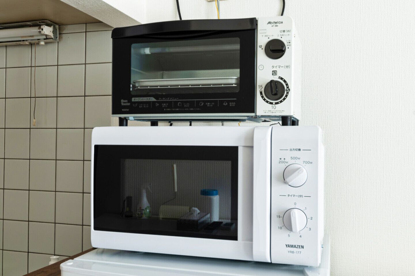 A kitchen with a black and white microwave oven stacked on top of a white microwave oven.