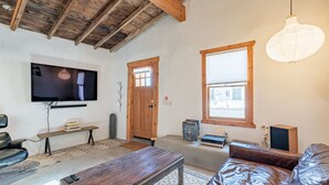 Una sala de estar con techo de madera, un televisor montado en la pared, un sofá, una mesa de centro y una ventana con persianas.