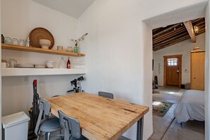 A compact kitchen with a wooden table, chairs, and shelves with kitchenware. - Modern Historic 1900 Adobe Bungalow in Downtown - Low Summer Rates! 🌇 (Tucson)