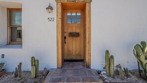 Una puerta de madera con el número '522' arriba, que da a una casa de fachada blanca y una ventana pequeña a la izquierda.