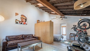 Amplia sala de estar con sofá de cuero, una mesa de centro de madera y un mueble aparador grande de madera. Una bicicleta está montada en la pared y hay un ventilador de techo.