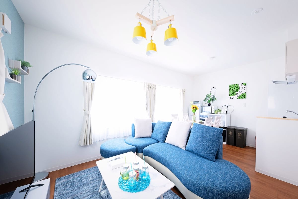 A modern living room with a blue sectional sofa, a white coffee table, and a kitchen area in the background.
