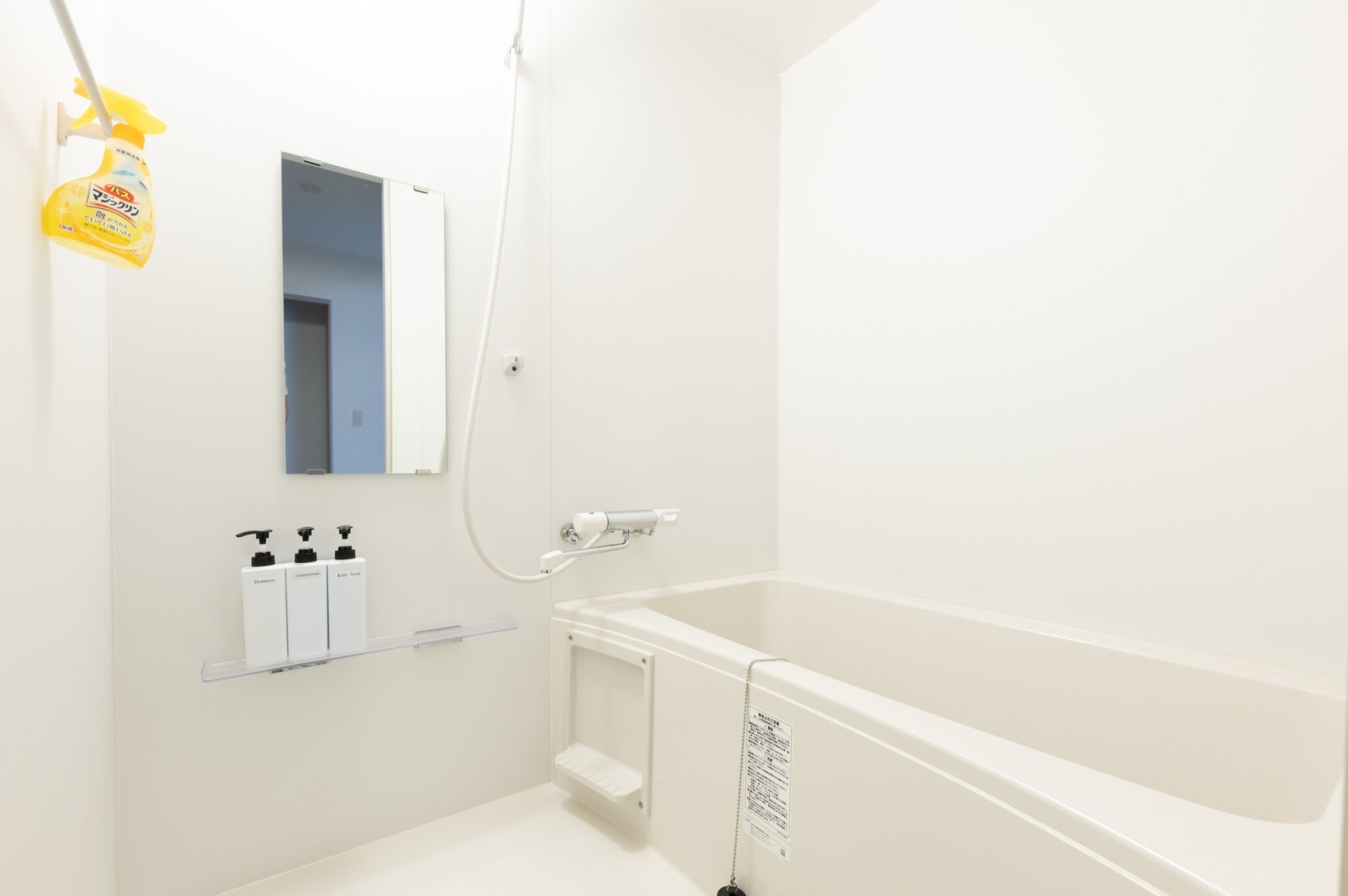 A white bathroom with a bathtub, a shower, and a mirror. There are three bottles of toiletries on a shelf.