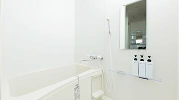 A modern bathroom with a bathtub, a shower, and a mirror. There are three bottles of toiletries on a shelf.