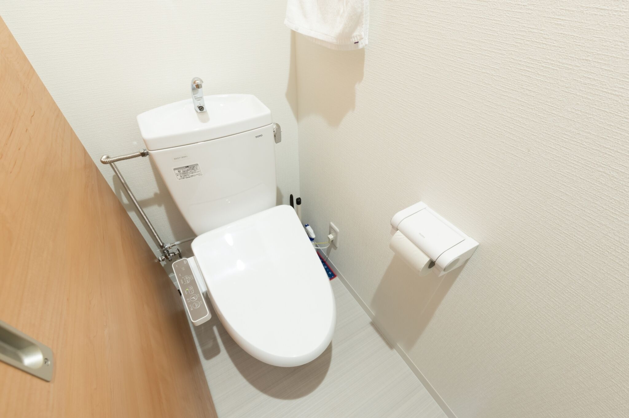 A modern toilet with a control panel, a toilet paper holder, and a wooden door.