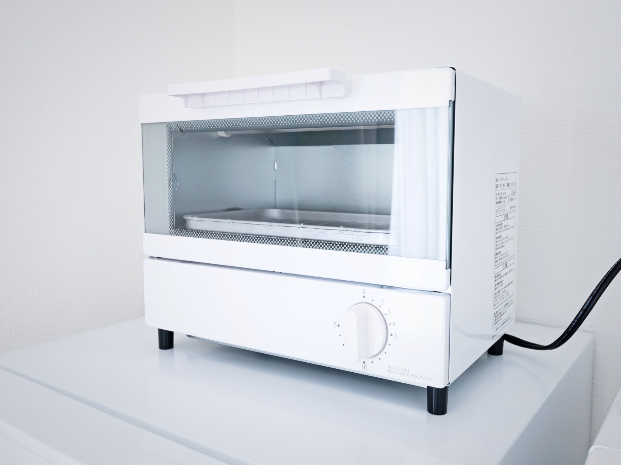 A white, compact, modern oven with a digital display and a control knob, placed on a white surface.