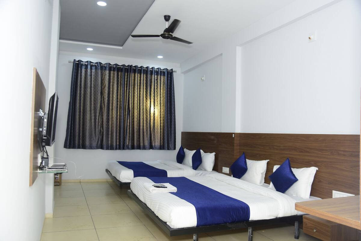 A hotel room with two beds, a wooden headboard, a ceiling fan, a TV, and a window with curtains.