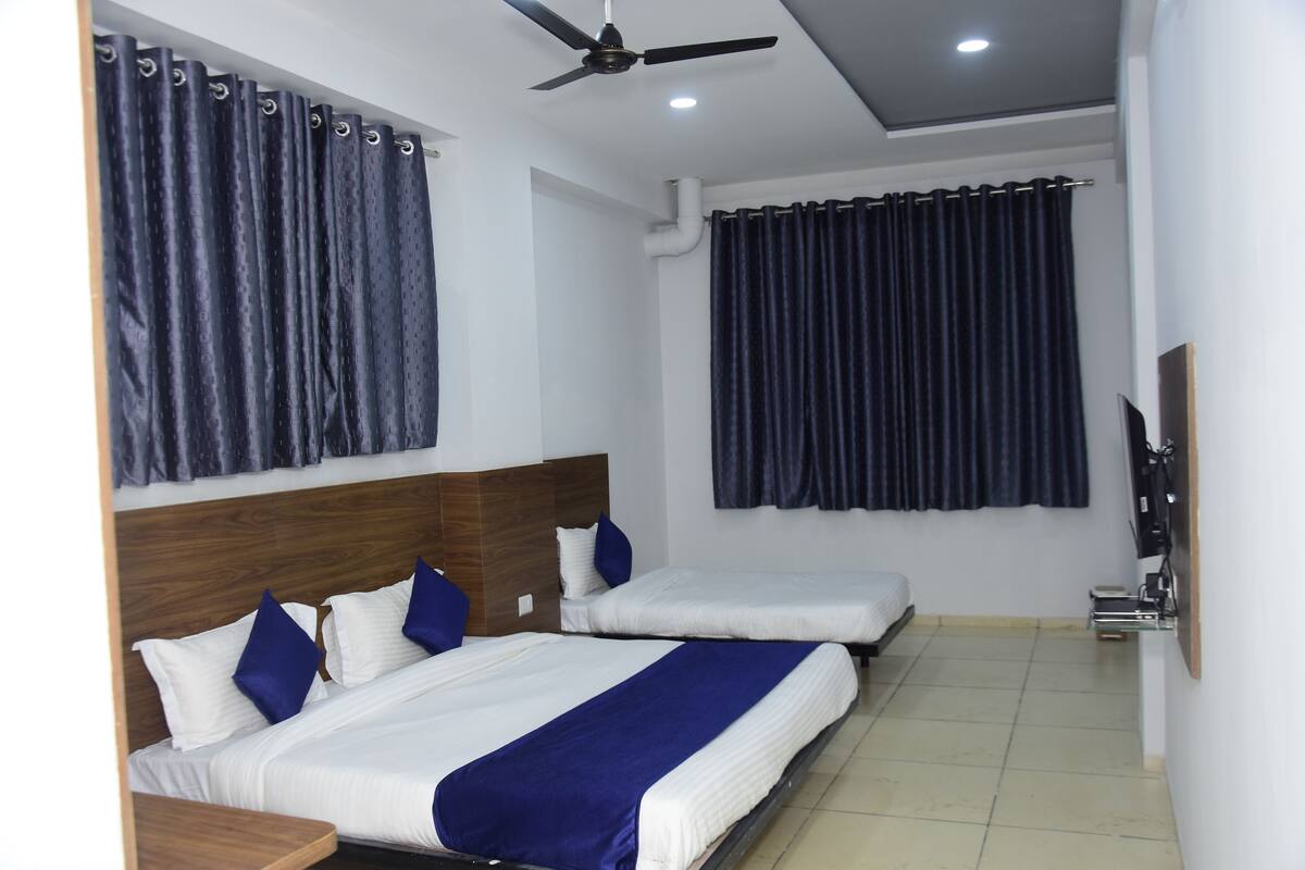 A hotel room with two beds, a ceiling fan, a TV, and a window with curtains.