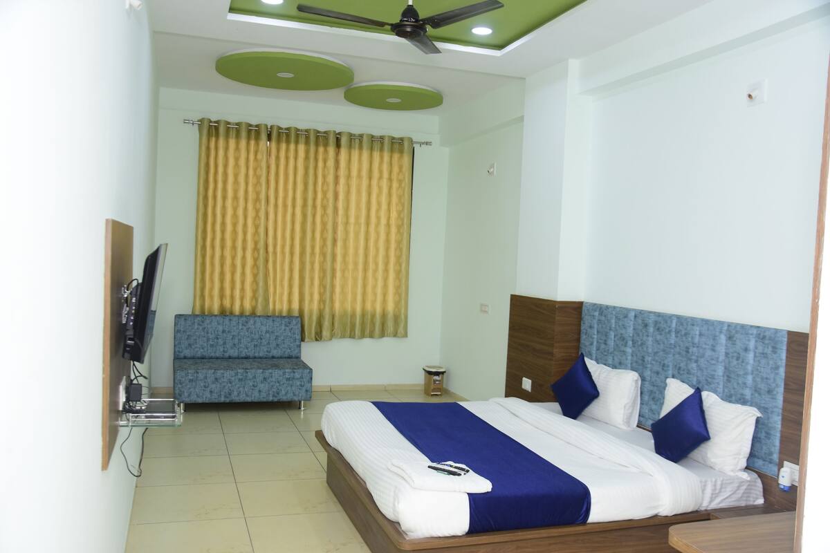 A hotel room with a bed, a TV mounted on the wall, a sofa, and a ceiling fan.
