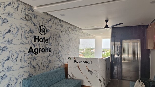 A hotel reception area with a marble wall, a reception desk, a blue sofa, and a ceiling fan.