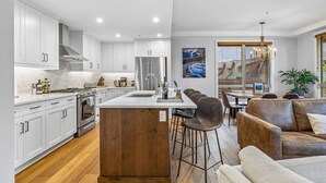 A modern kitchen with white cabinets, a central island, and stainless steel appliances. - Stay in Style | Mountain Scene (Canmore)