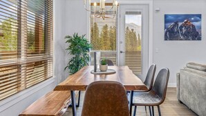 A dining area with a wooden table, chairs, and a chandelier. - Stay in Style | Mountain Scene (Canmore)