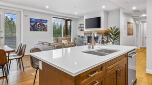 A modern kitchen with a large island, wooden cabinets, and a built-in TV. - Stay in Style | Mountain Scene (Canmore)