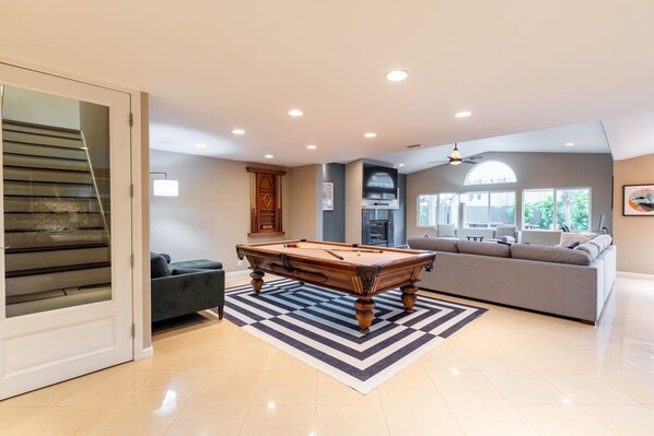 A modern living room with a pool table, a sofa, and a staircase.