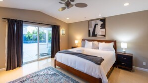 Een hotelkamer met een groot bed, een plafondventilator, uitzicht door de glazen deur en een nachtkastje met een lamp.