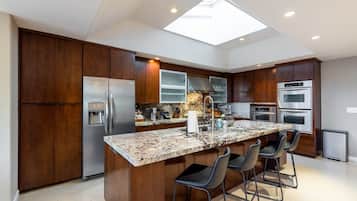 A modern kitchen with a central island, bar stools, a built-in oven, and a skylight.