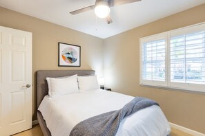 Et soveværelse med en seng, ventilator, et vindue med persienner og en dør.