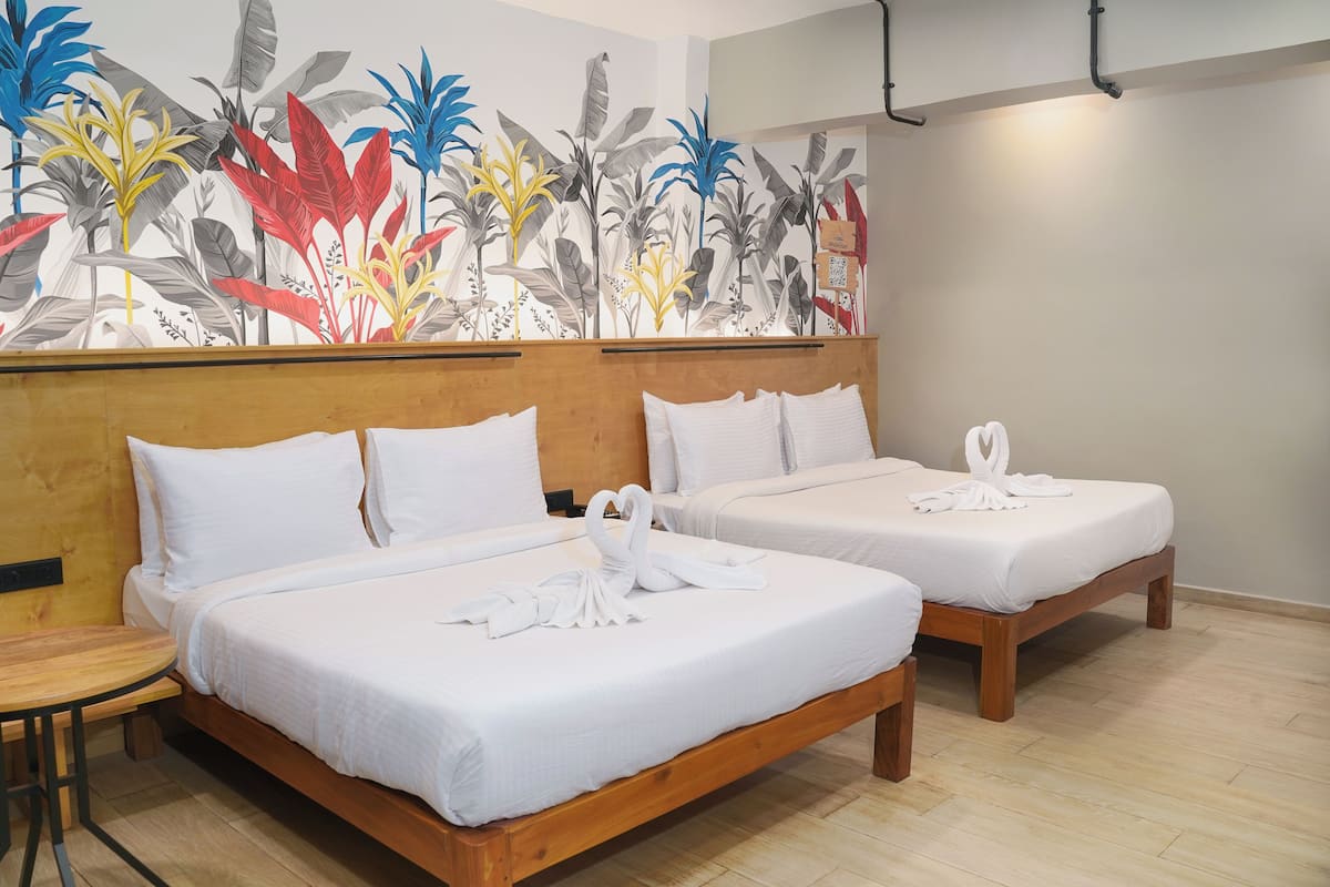 Two single beds with white linens and towels, a wooden headboard, and a tropical plant mural on the wall.