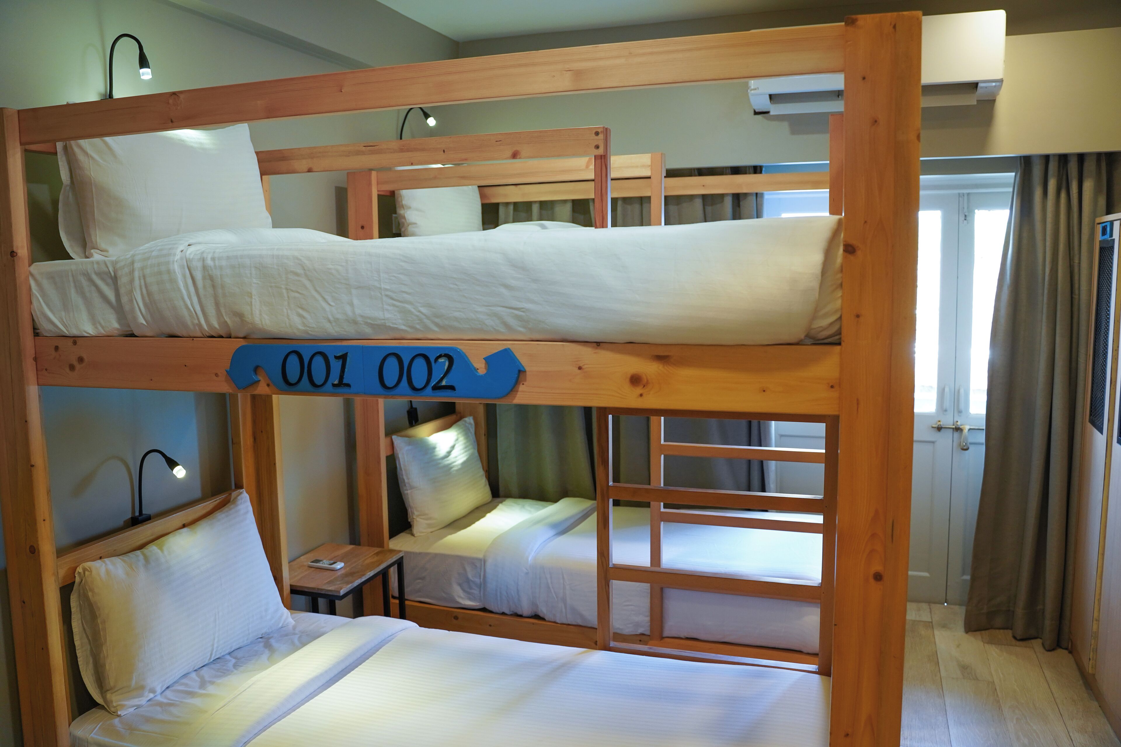 A bunk bed room with three beds, each with a pillow and a small table.