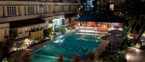 A nighttime view of a hotel with a swimming pool, outdoor seating, and well-lit pathways.