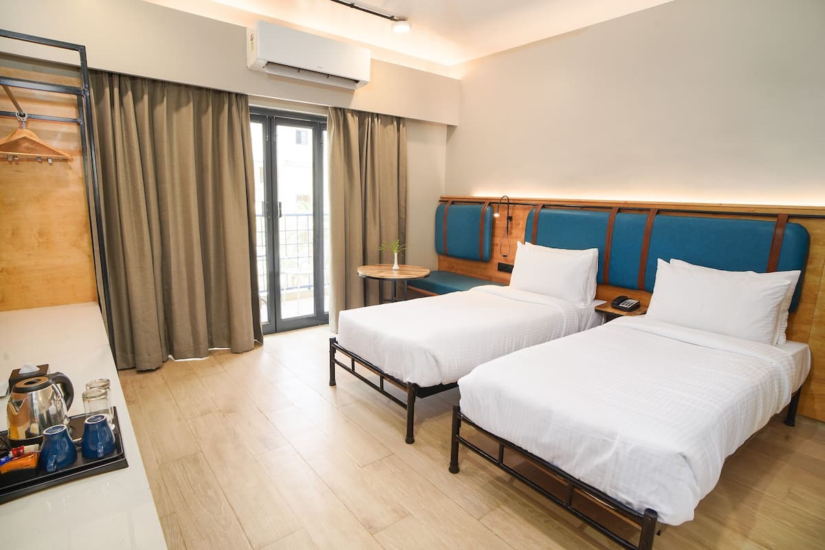 A hotel room with two beds, a wooden headboard, a small table with a plant, and a window with curtains.