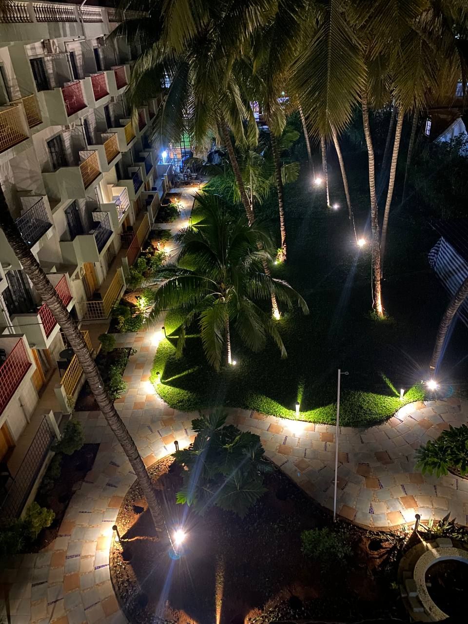Ein mehrstöckiges Hotel mit Balkonen, einem angelegten Garten mit Palmen und einem gepflasterten Weg.