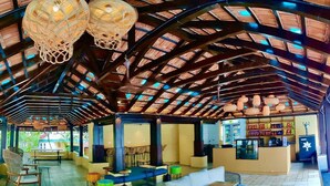 An indoor space with a high ceiling, wooden beams, and hanging lamps. There are tables and chairs arranged for seating. - Indie Stays Goa (Candolim)