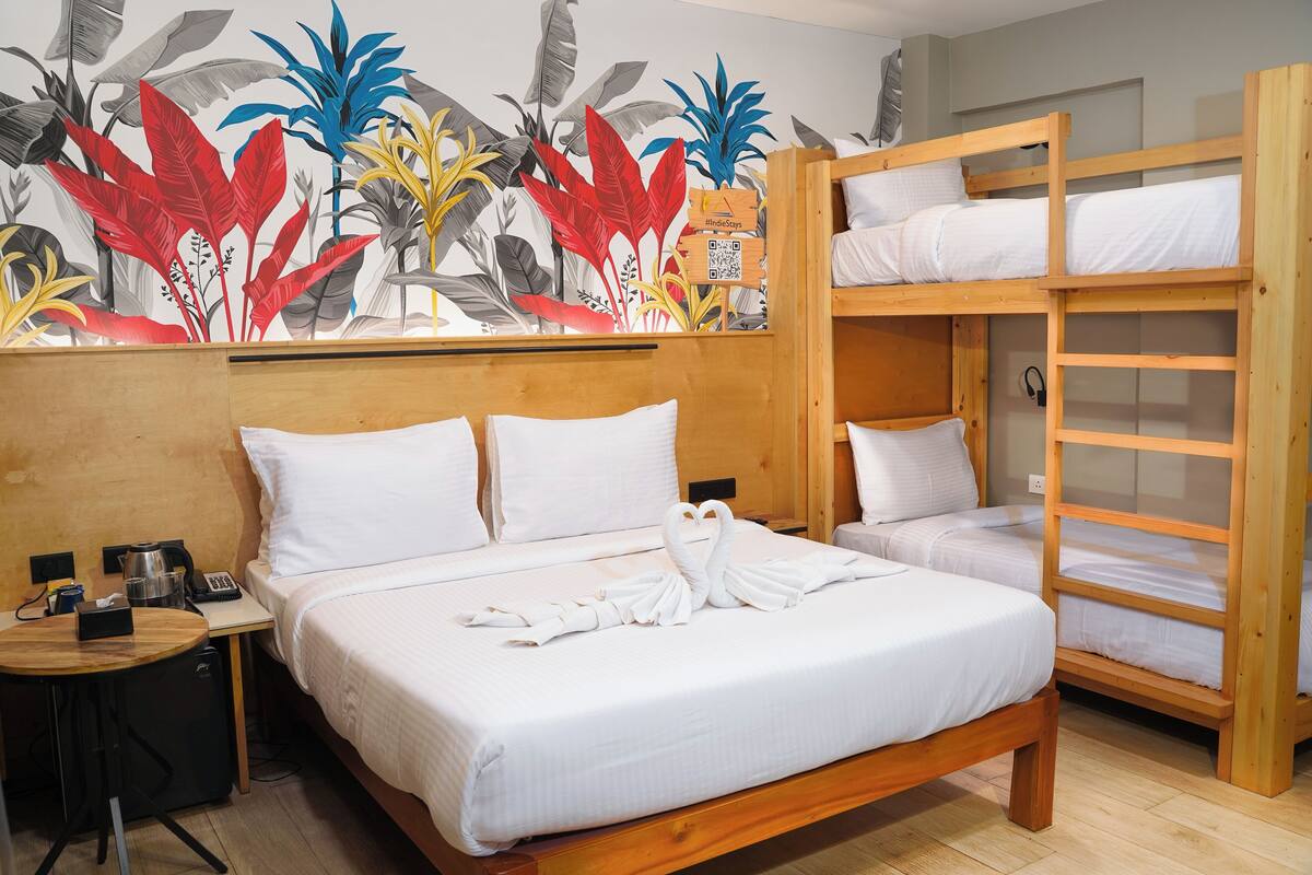 A hotel room with a large bed, a smaller bed, a desk with a phone, and a wall with a tropical mural.