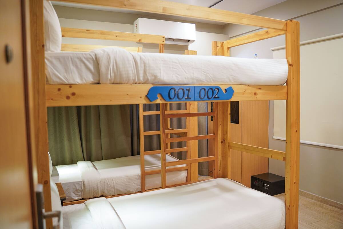 A bunk bed with two levels, each with white bedding. There is a blue sign with numbers "001 002" on the middle bunk.