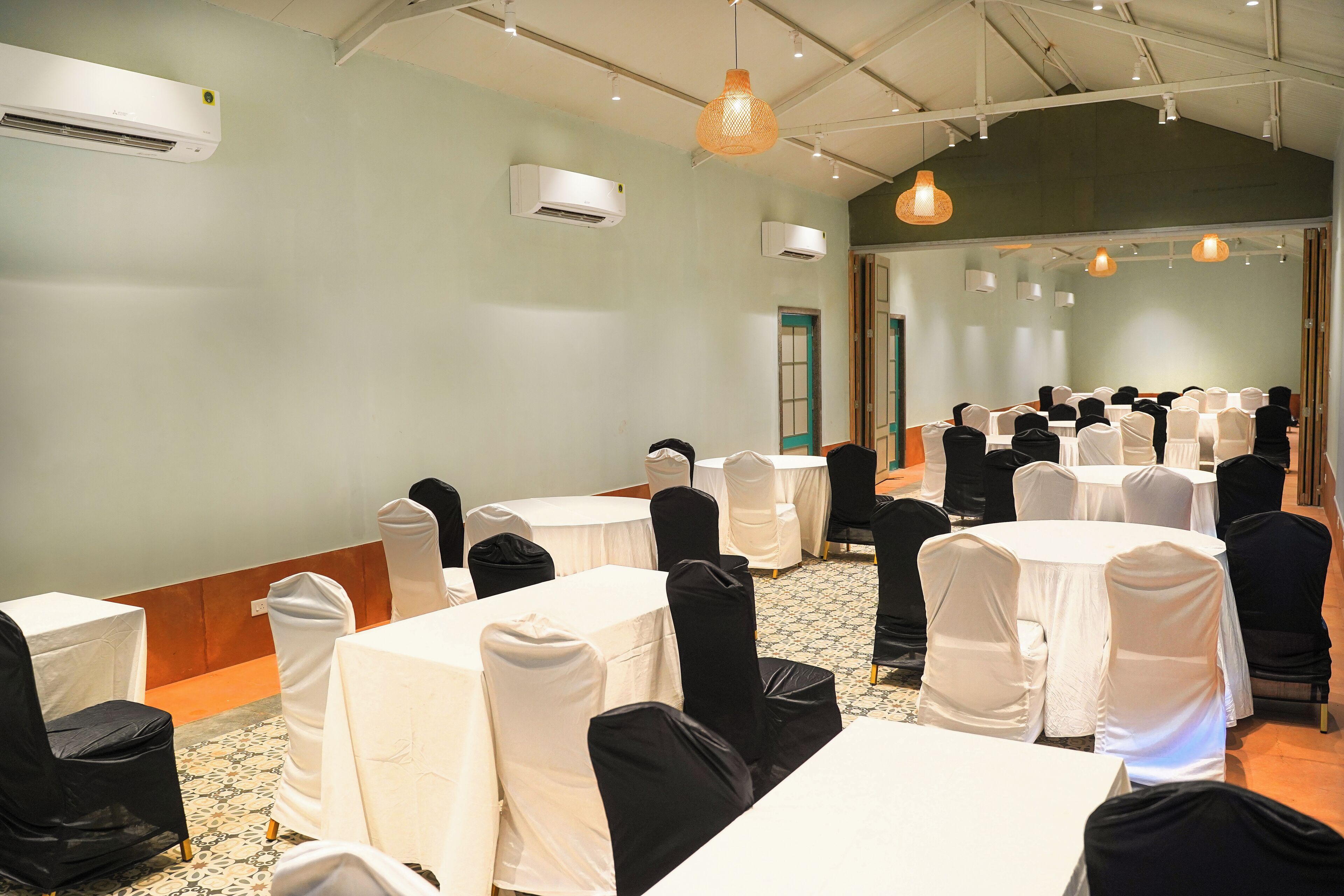 Un salón de conferencias con mesas y sillas, unidades de aire acondicionado e iluminación colgante.