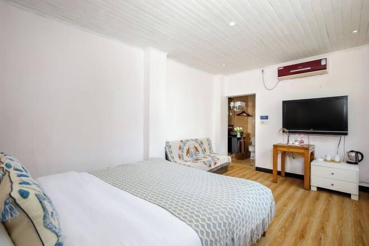 A hotel room with a bed, a TV, a desk with a chair, and a wardrobe.