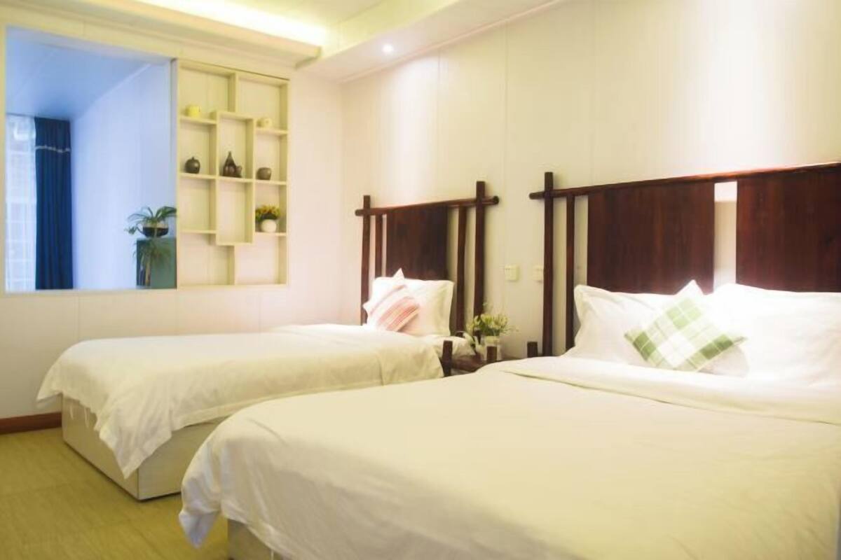 A hotel room with two beds, a window with a view, a shelf with decorative items, and a wooden headboard.