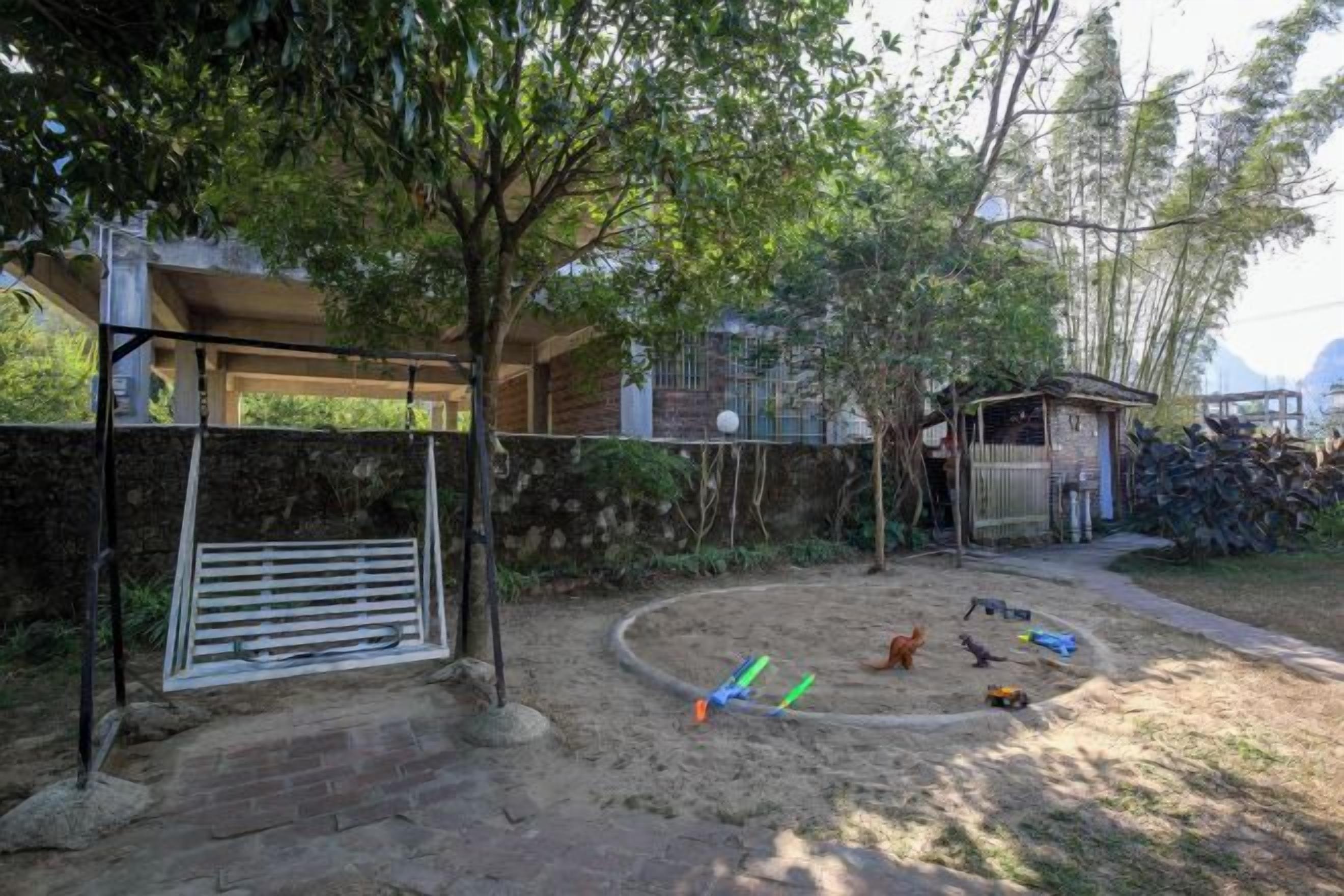 Patio trasero cercado con zona de juegos de arena, un cobertizo pequeño y un árbol que da sombra.