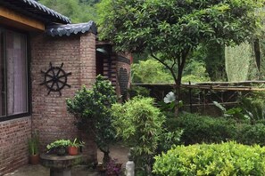 A brick building with a ship's wheel decoration, surrounded by lush greenery and a wooden fence. - Yangshuo Xingping Our Inn-Near 20 Yuan Background (Yangshuo)