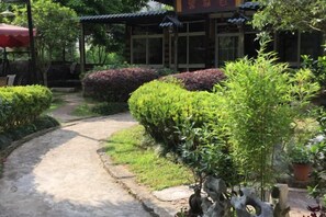 A pathway leading to a traditional building with a tiled roof, surrounded by well-maintained hedges and potted plants. - Yangshuo Xingping Our Inn-Near 20 Yuan Background (Yangshuo)