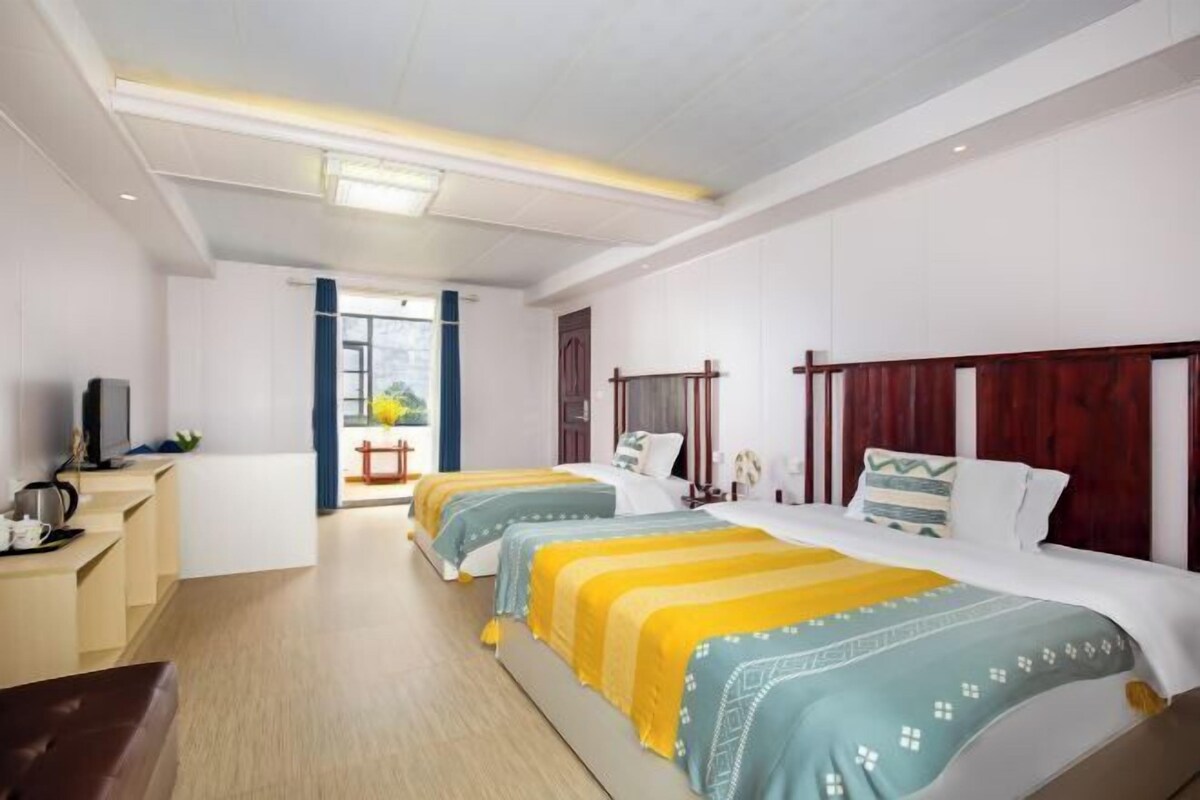 A hotel room with three beds, a desk with a chair, and a television.