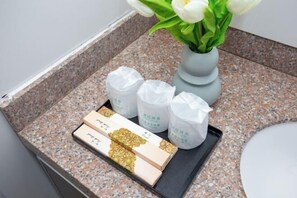 A bathroom counter with a vase of white flowers, a tray with boxes and bottles, and a granite countertop.