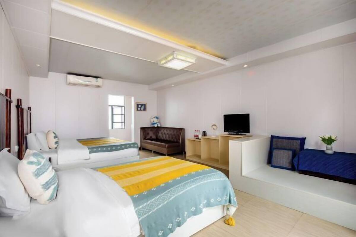 A hotel room with two beds, a sofa, a TV, and a small desk.