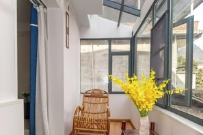 A room with a large window, a wicker chair, a vase with yellow flowers, and a wooden table. - Yangshuo Xingping Our Inn-Near 20 Yuan Background (Yangshuo)