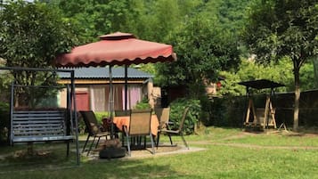 A covered outdoor seating area with a table and chairs, a swing set, and a fenced play area.
