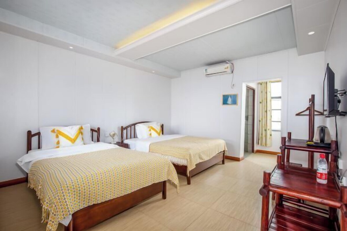 A hotel room with two beds, a TV, a wooden table, and an air conditioning unit.