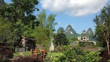A rural setting with a small wooden structure, a paved path, and a view of mountains in the distance.