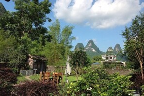 A rural setting with a small wooden structure, a paved path, and a view of mountains in the distance. - Yangshuo Xingping Our Inn-Near 20 Yuan Background (Yangshuo)