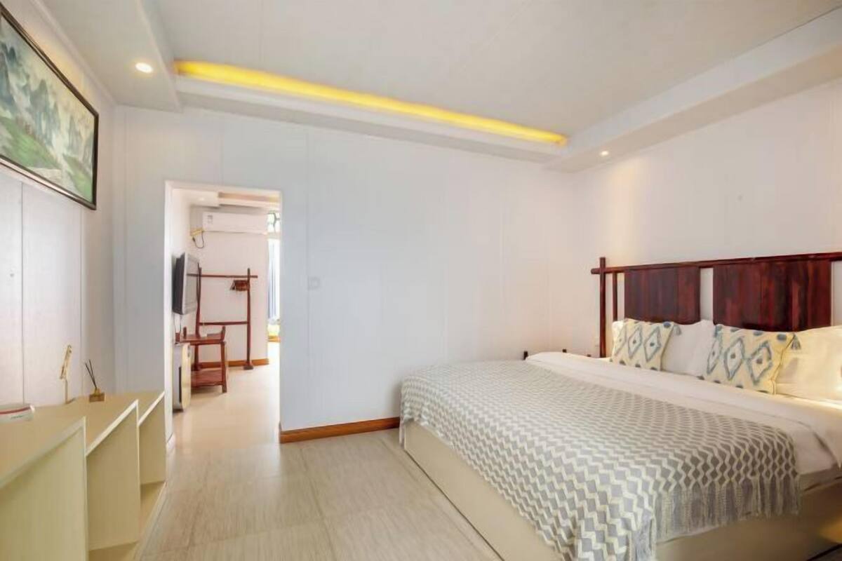 A bedroom with a bed, bedside tables, a TV, and a door leading to another room.