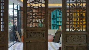 A room with a checkered tablecloth, a bed with a white blanket, and a view of a blue and yellow bookshelf through a wooden partition with intricate designs. - Yangshuo Xingping Our Inn-Near 20 Yuan Background (Yangshuo)