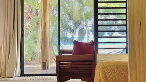 Une pièce avec un lit, une chaise en bois et une vue sur les arbres, visible à travers une porte-fenêtre coulissante.