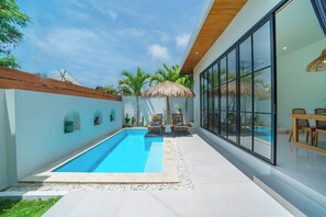 A modern pool area with a clear blue pool, lounge chairs, and a thatched umbrella. - Villa Selina (Canggu)