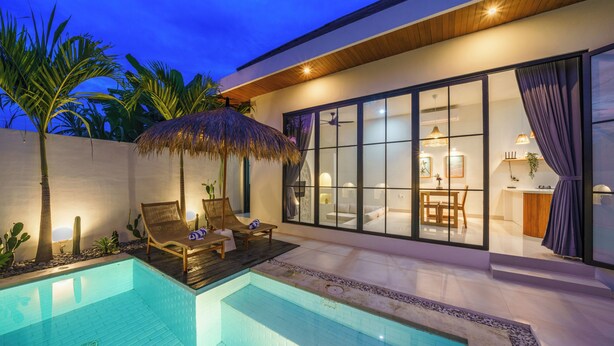 Un área de piscina moderna con una sala acristalada, un quiosco de paja y una terraza de madera.