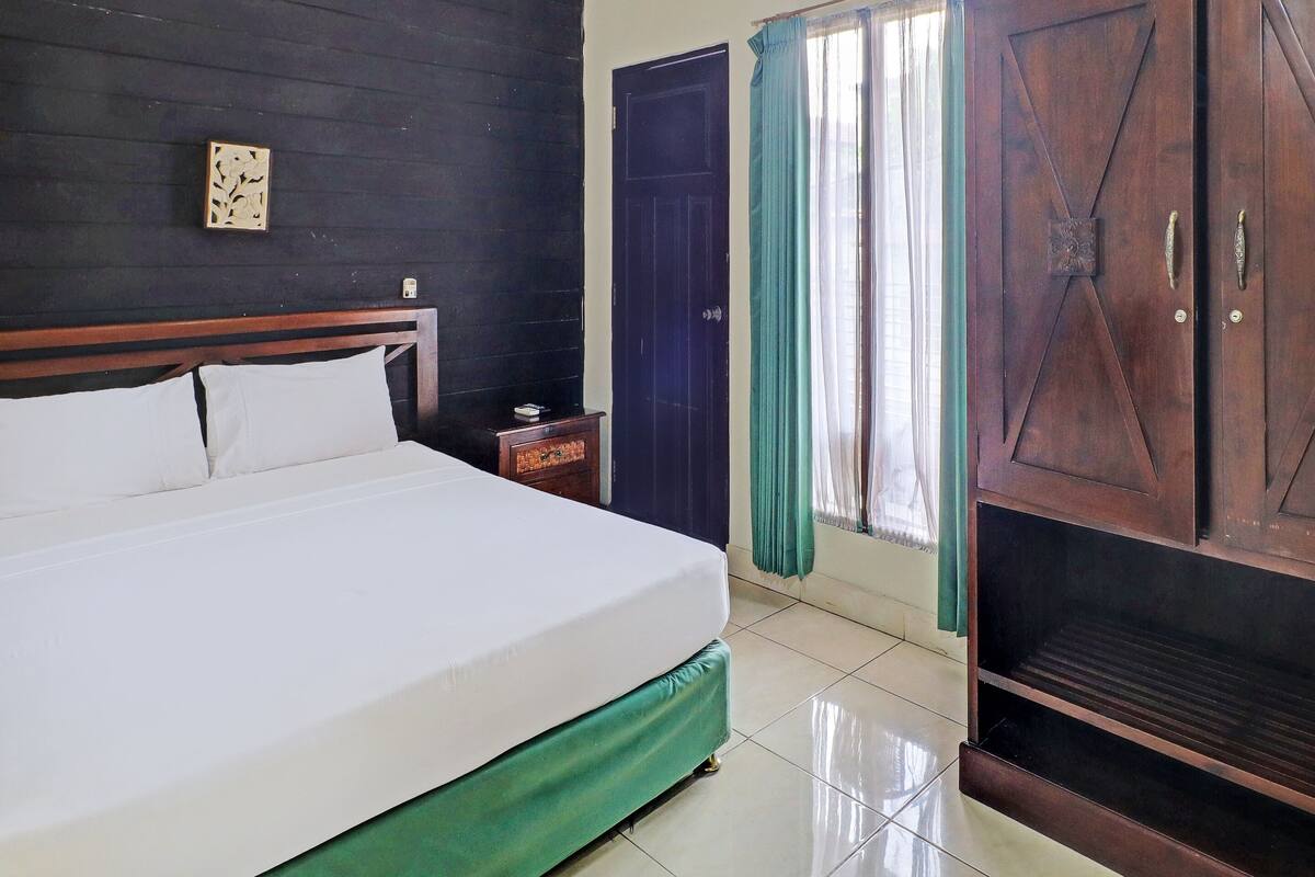 A neatly made bed with white linens, a wooden headboard, a small bedside table with a book, and a dark wooden wardrobe.