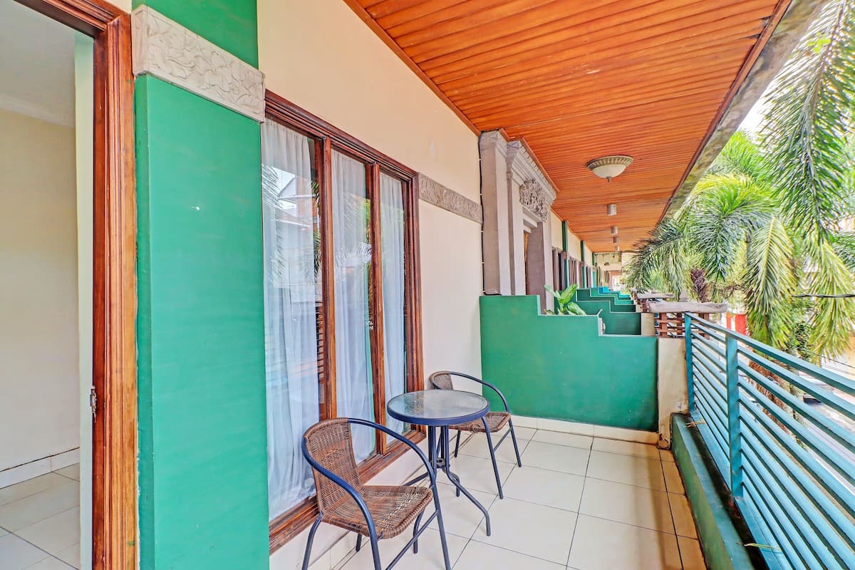 A balcony with two wicker chairs, a small table, and a green wall with a window.